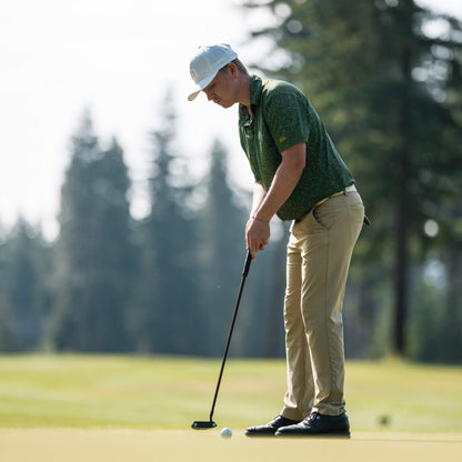 A person wearing a cap and green shirt is putting on a golf course.